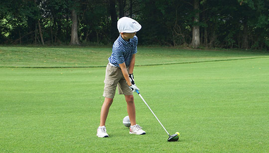 Young boy teeing off on a fairway
