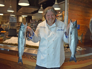 Bill Ranniger holding two salmon in front of oyster bar at Bellevue Duke's Seafood